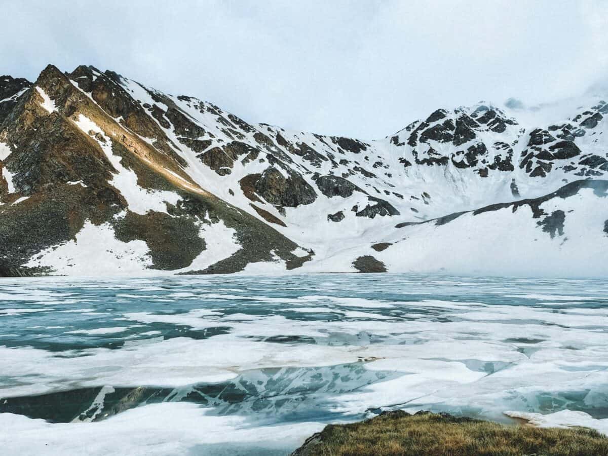 Superbe lac gelé entouré de montagnes enneigées, capturant le paysage hivernal serein.
