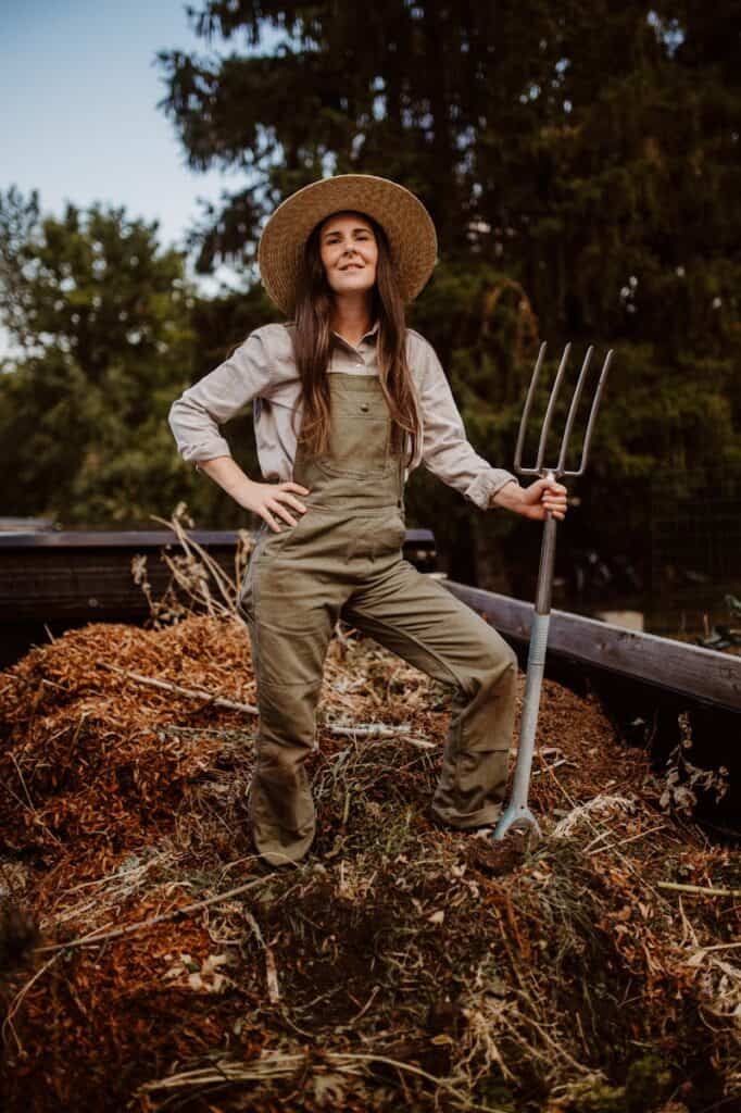Femme jardinière fièrement debout avec une fourche près d'un tas de compost à l'extérieur.