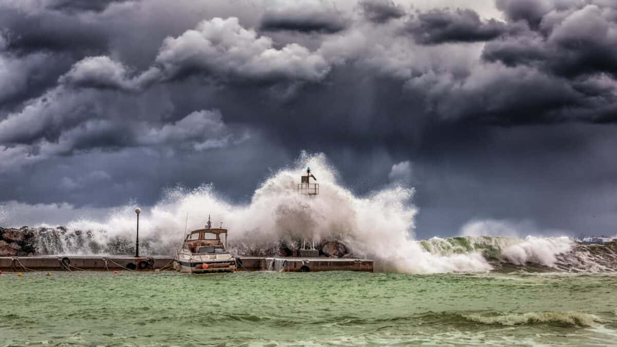 De puissantes vagues s'écrasent contre une jetée et un phare sous un ciel sombre et orageux.